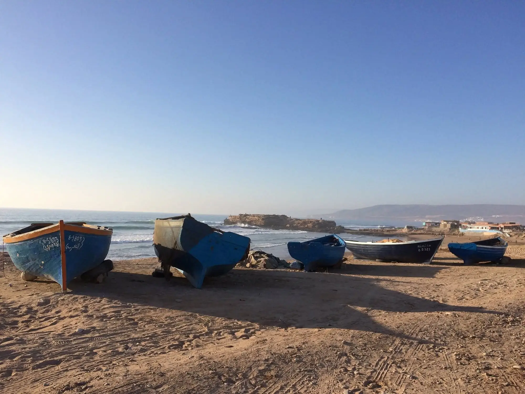 Blue fishing boats pulled up on the beach, with the Atlantic surf behind