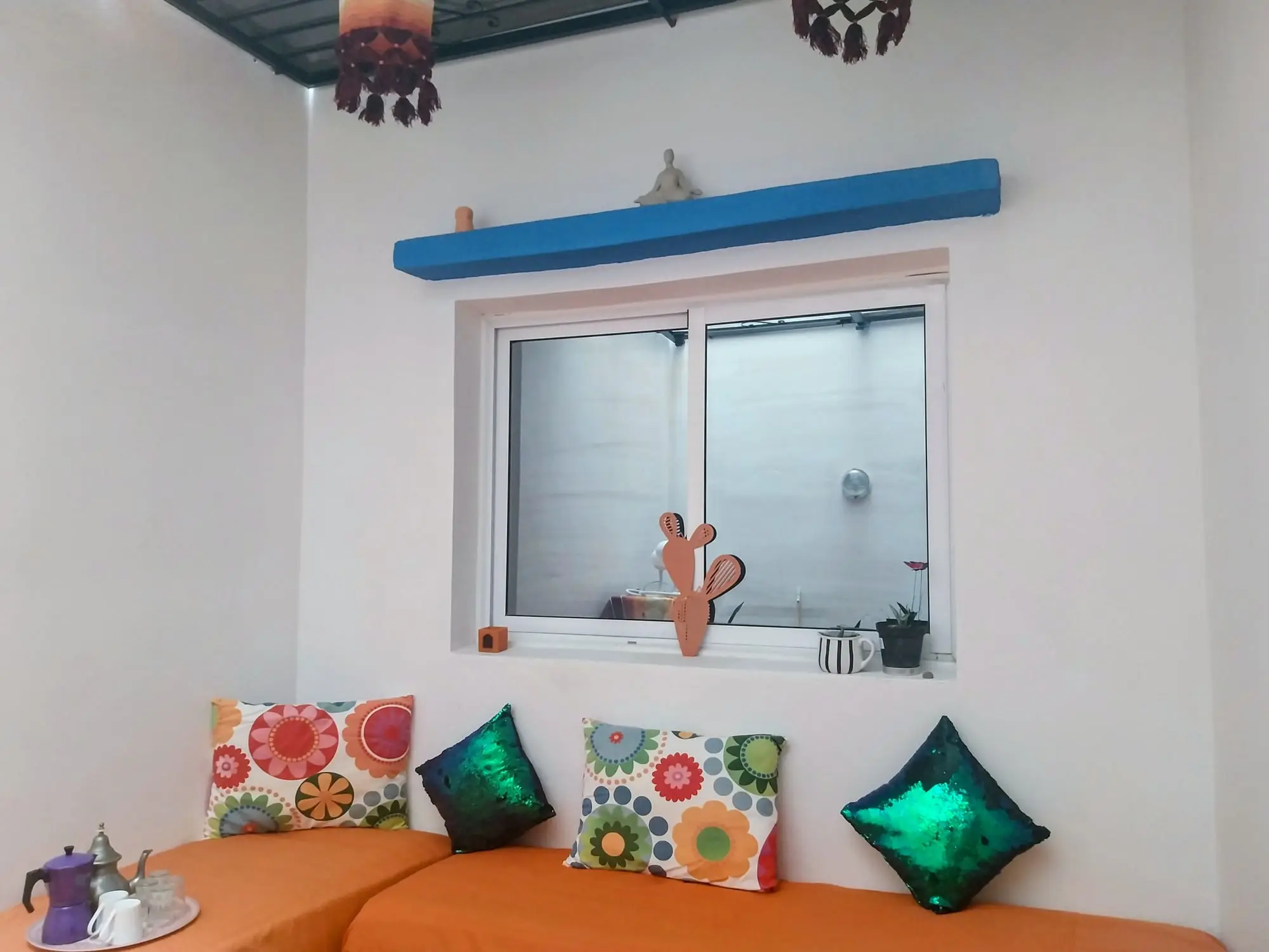 Bench seating with bright cushions beneath a window, with a blue shelf above