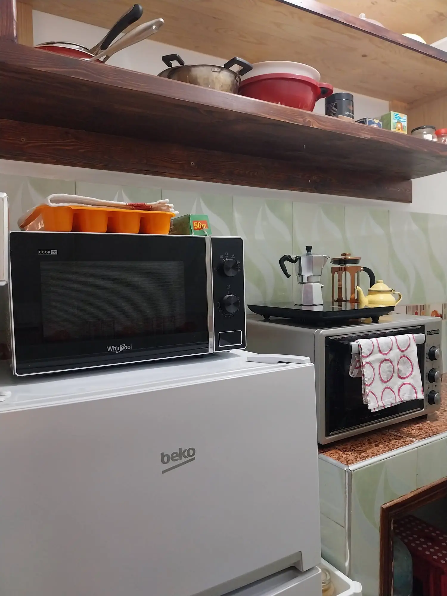 Kitchen corner with a microwave, fridge, kettle and shelves of pans