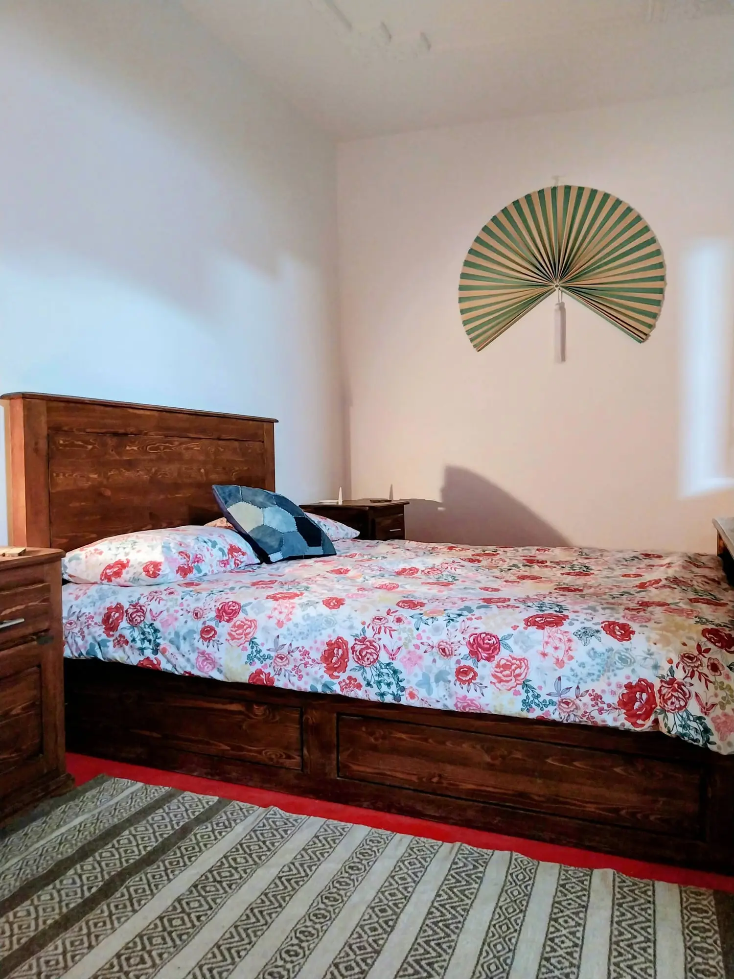 Double bed with a floral bedspread beneath a woven palm fan