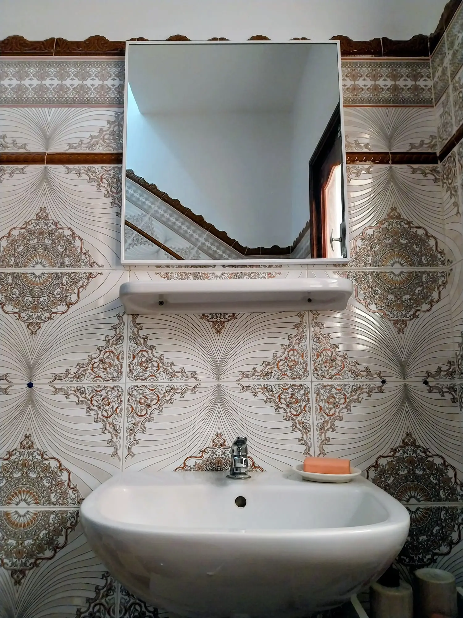 Bathroom washbasin and mirror against patterned tiles
