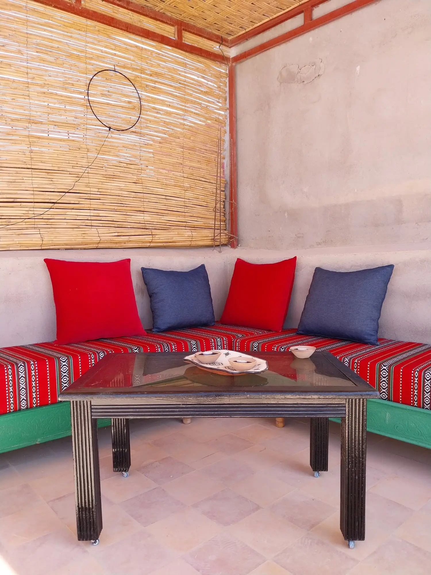 Shaded terrace bench with red and blue cushions and a low table