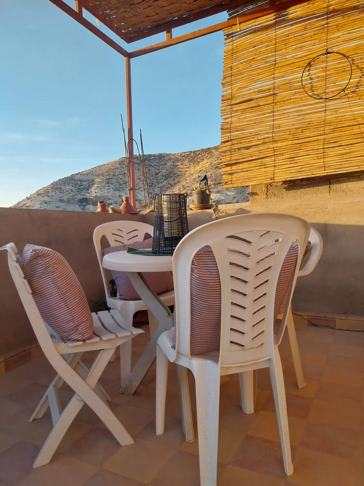 Terrace table and chairs beside a reed screen, with the hills behind